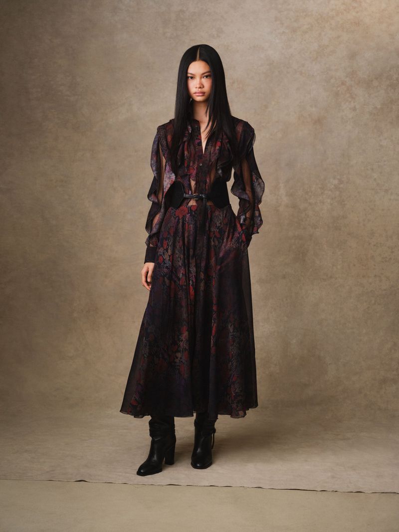 Full-length shot of an Asian woman with long dark hair posing in a long-sleeve patterned dress and black boots against a neutral background.