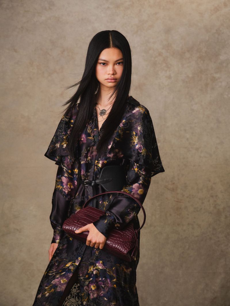 Fashion shot of a woman with long dark hair wearing a floral dress, black belt, and carrying a burgundy crocodile-patterned purse.