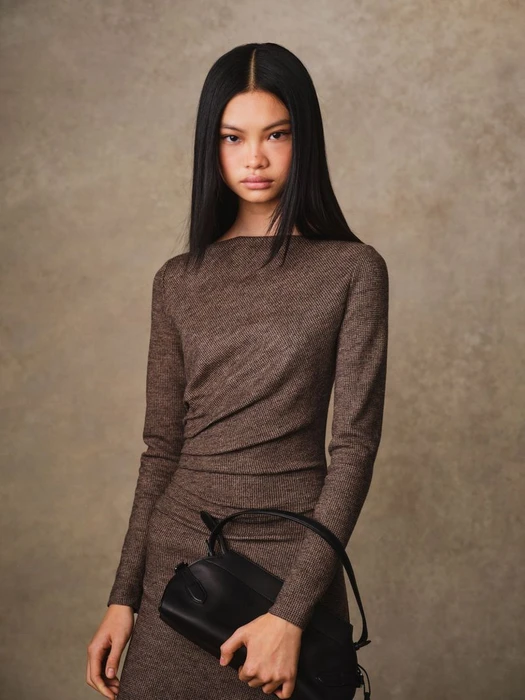 Model Yue Gu wearing a brown textured dress holding a black handbag against a mottled textured background for Ralph Lauren Fall 2025.