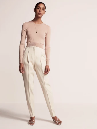 Fashion portrait of a woman wearing a light pink sweater and cream-colored trousers with strappy sandals in a studio setting.