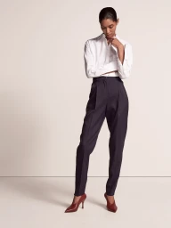 Model wearing a white shirt and dark trousers against a minimalist studio background