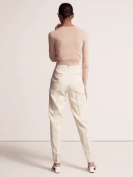 Model seen from behind wearing a fitted nude long-sleeve knit top and tailored cream high-waisted trousers against a studio backdrop.