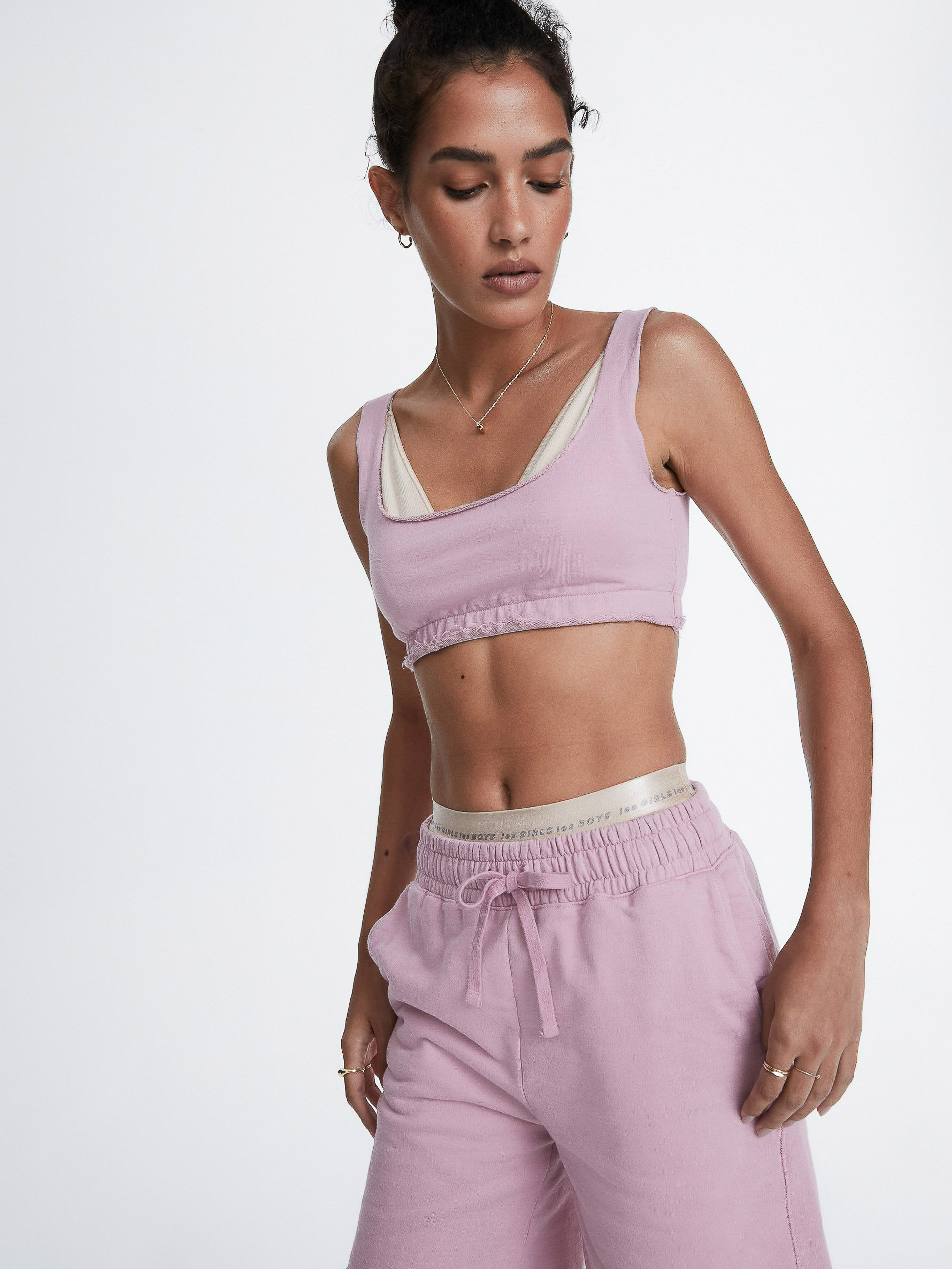Athletic woman in pink sports bra and sweatpants poses against a white backdrop, showcasing sporty fashion in a bright studio shot.