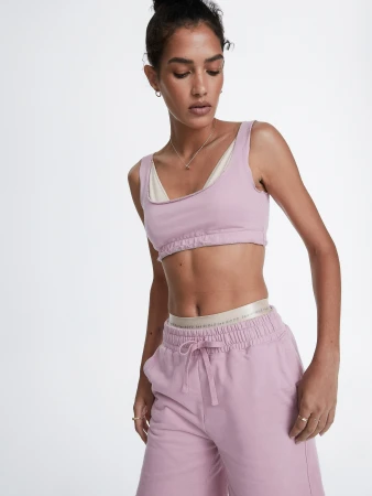 Athletic woman in pink sports bra and sweatpants poses against a white backdrop, showcasing sporty fashion in a bright studio shot.