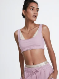 Model wearing a pink athletic crop top and matching sweatpants against a white background by Slate Studios for Bandier.