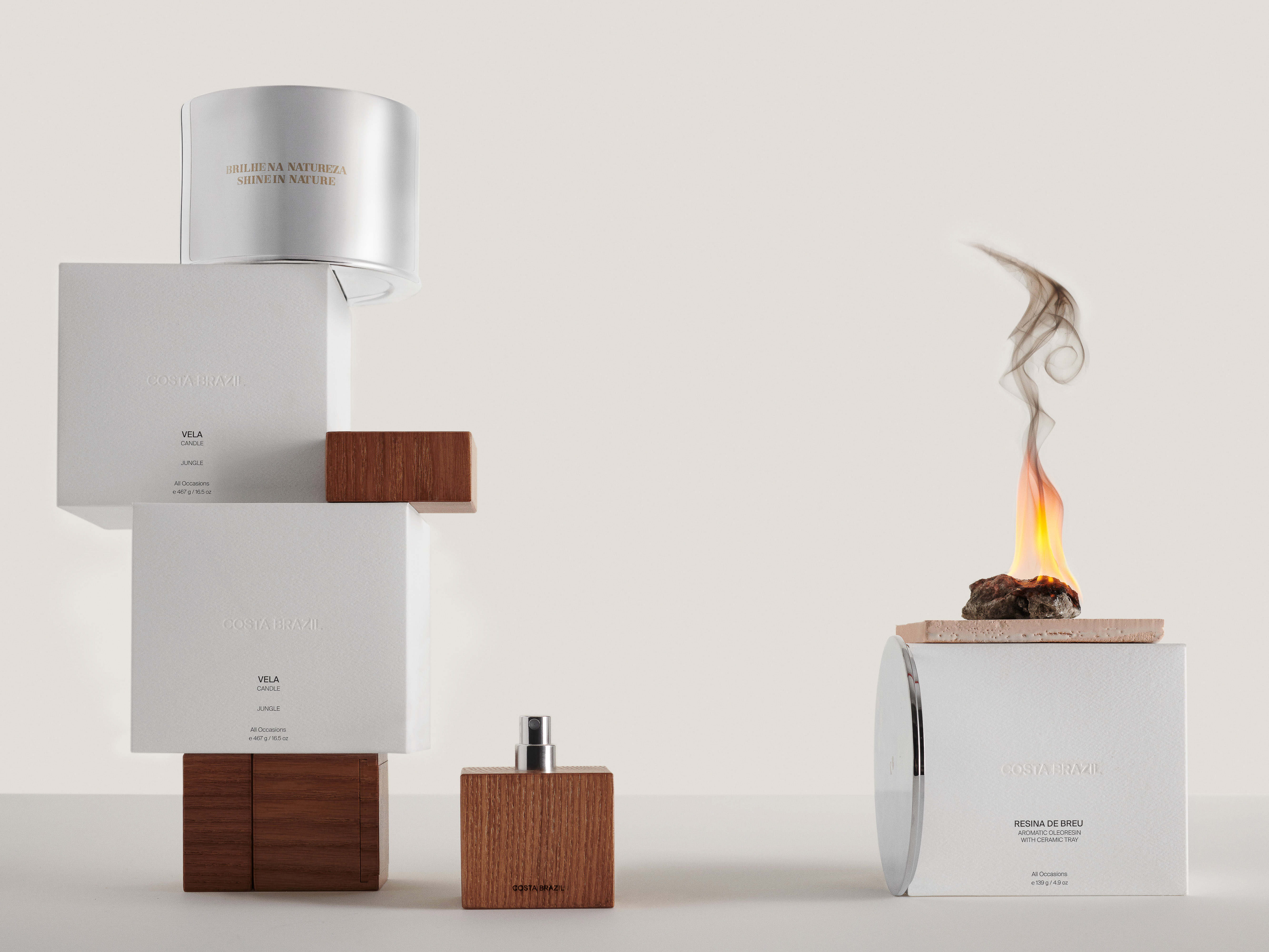 Still life shot of Costa Brazil home fragrance products including perfume, candle, and diffuser with minimalist packaging on a beige background.