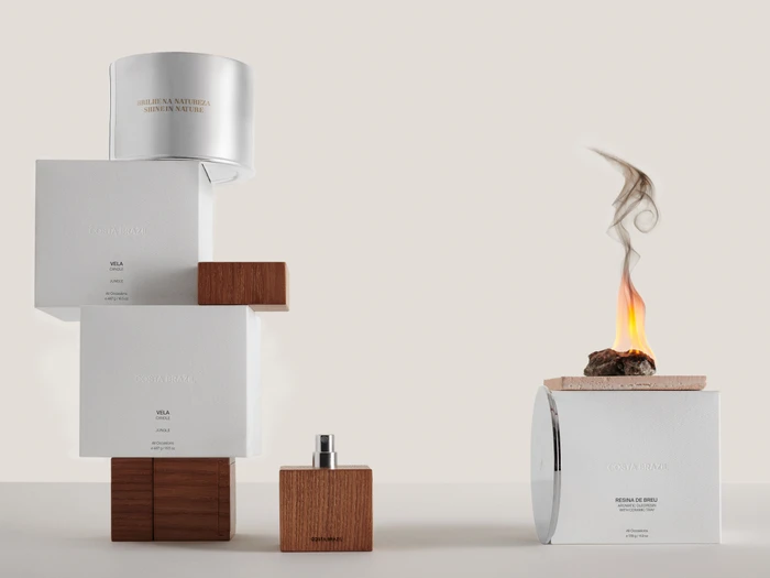 Costa Brazil beauty product packaging with stacked white boxes, wooden perfume bottle, and a burning resin block on tile