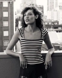 Woman in striped top leaning against rooftop ledge with city buildings in background