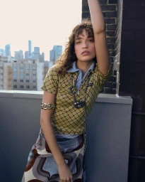 Woman in yellow patterned collared shirt standing on a rooftop with city skyline backdrop
