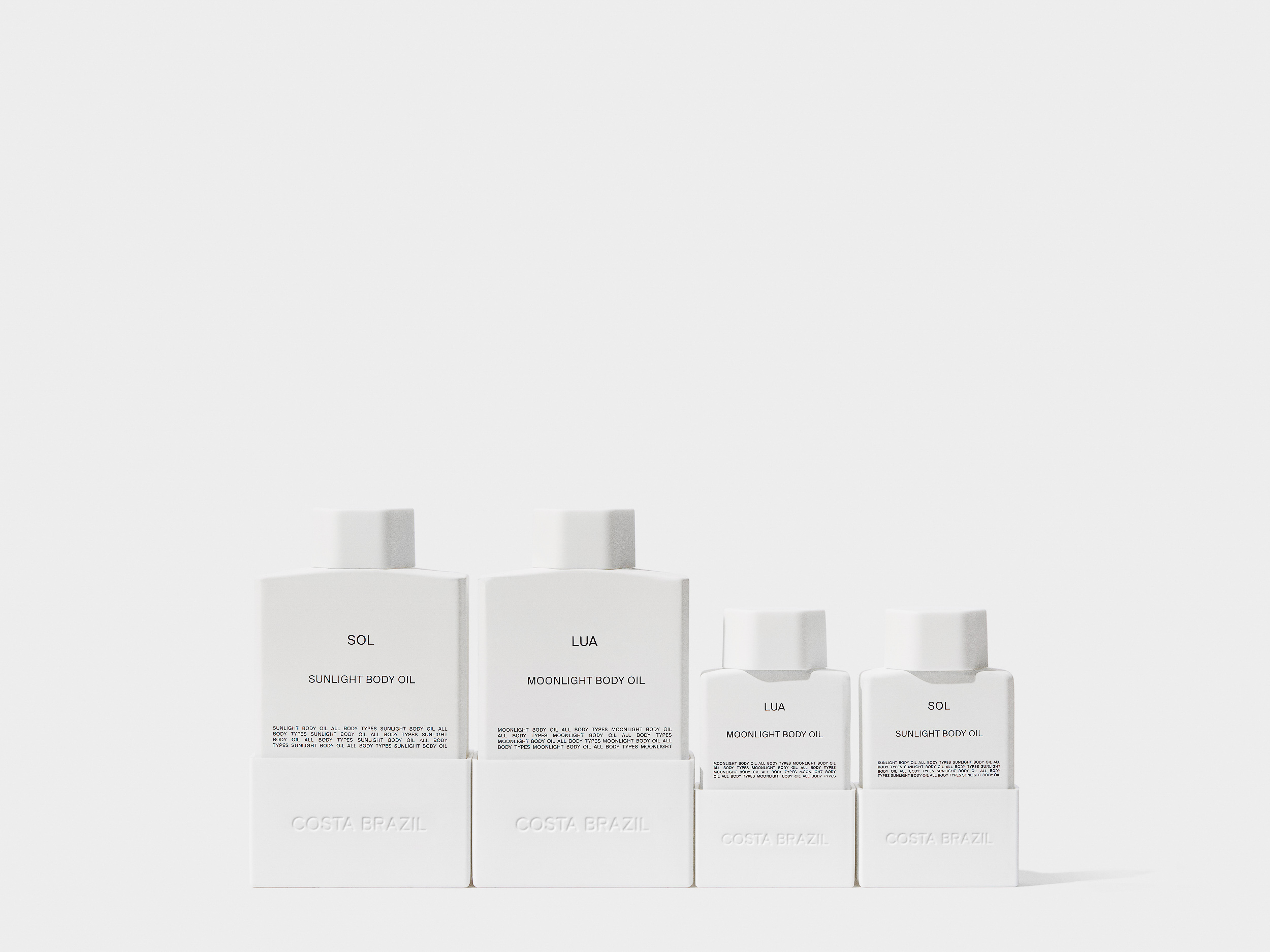Product shot showcasing four Costa Brazil body oil bottles in varying sizes, arranged on a white surface with minimalist white background.