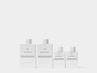 Four white Costa Brazil body oil bottles of varying sizes arranged on a white seamless background.