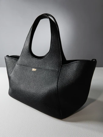 Black DKNY tote bag on a light gray surface against a dark gray background, showcasing its texture and design.