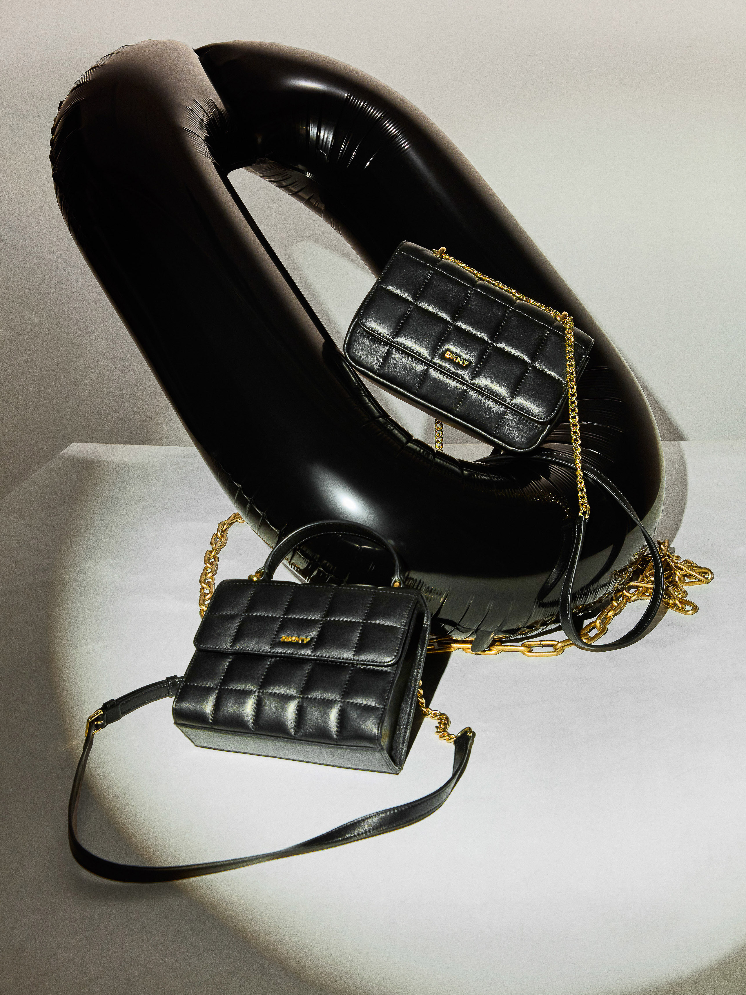 Two quilted black leather purses with gold chain straps are displayed alongside a large black inflatable ring on a white surface.