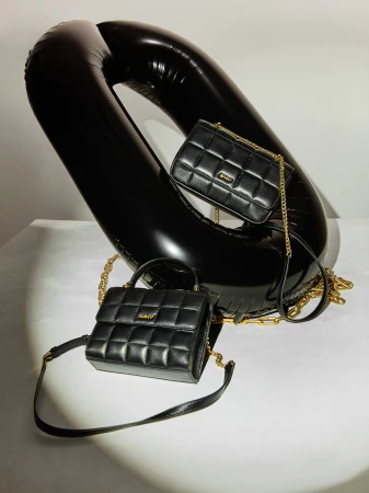 Two quilted black leather purses with gold chain straps are displayed alongside a large black inflatable ring on a white surface.