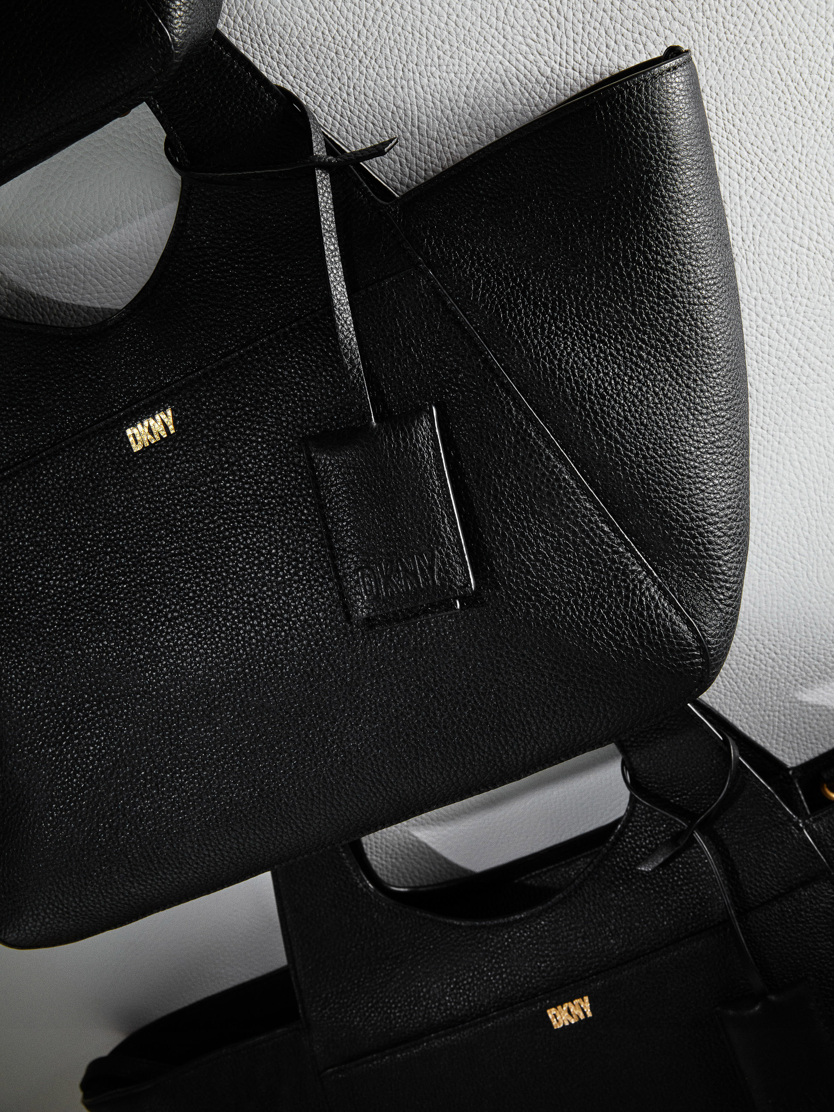 Close-up shot of two black DKNY handbags with a textured leather finish against a white background, showcasing fashion and brand identity.