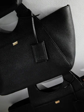 Close-up shot of two black DKNY handbags with a textured leather finish against a white background, showcasing fashion and brand identity.