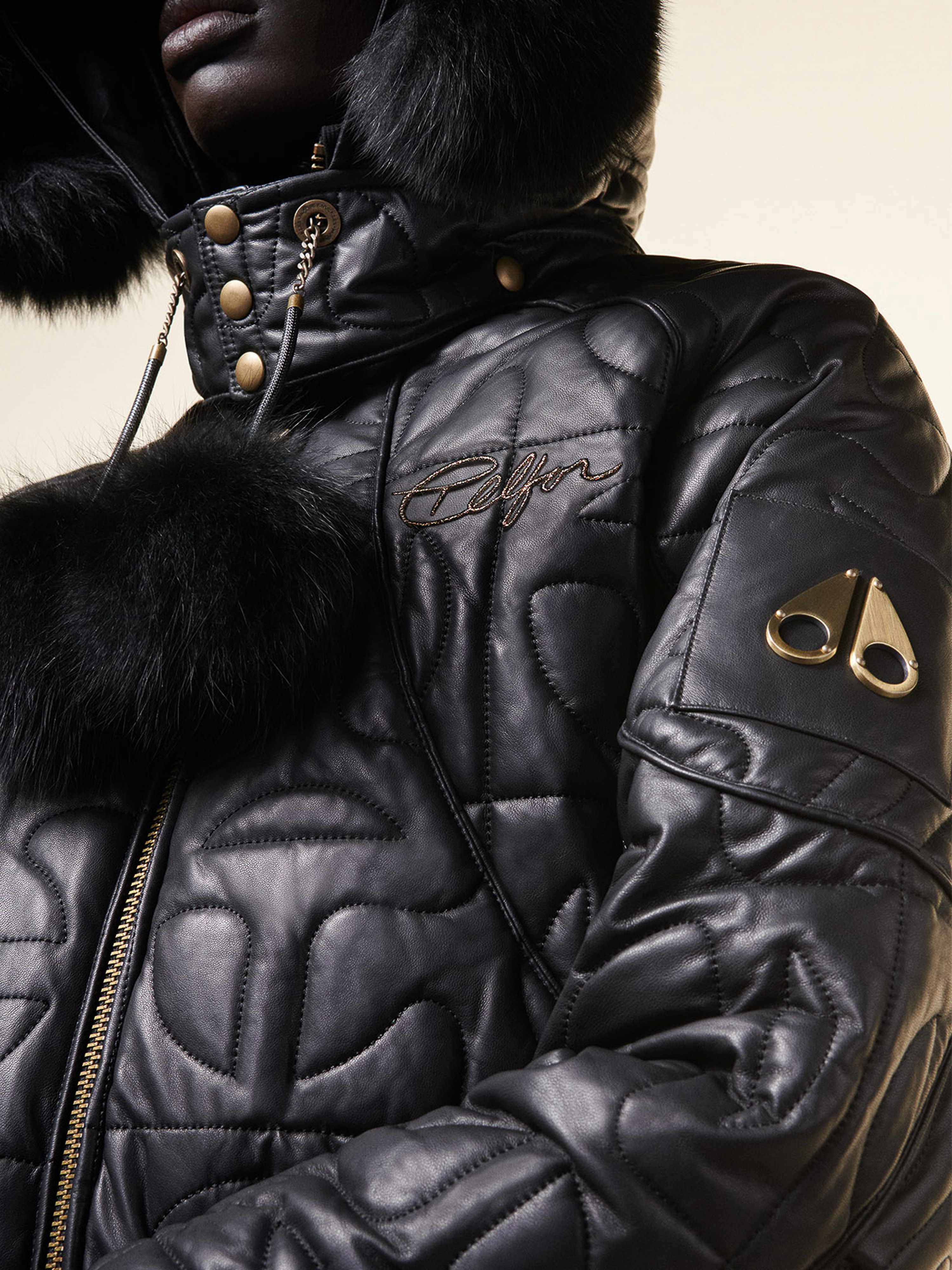 Close-up of a person in a black, quilted, fur-trimmed hooded jacket with metal hardware details, showcasing fashion and design.