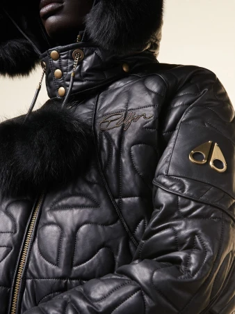 Close-up of a person in a black, quilted, fur-trimmed hooded jacket with metal hardware details, showcasing fashion and design.