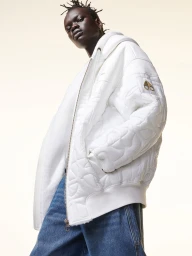 Model wearing a white puffer jacket and blue jeans against a plain background for Moose Knuckles