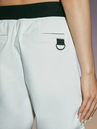 Close-up of a fair-skinned woman in white pants with a dark trim, featuring a unique textured manicure and a contemporary minimalist style.