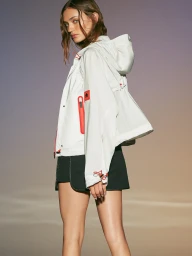 Model wearing a white hooded jacket with red accents and dark shorts against a gradient background.