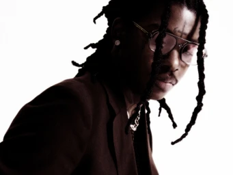 Portrait of a black man wearing glasses and a dark blazer against a bright white background