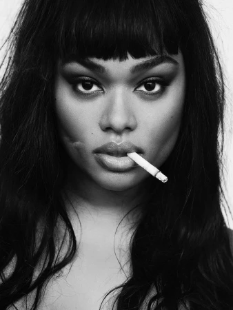 Close-up portrait of an adult woman with dark hair smoking a cigarette, set against a bright background in a monochrome aesthetic.