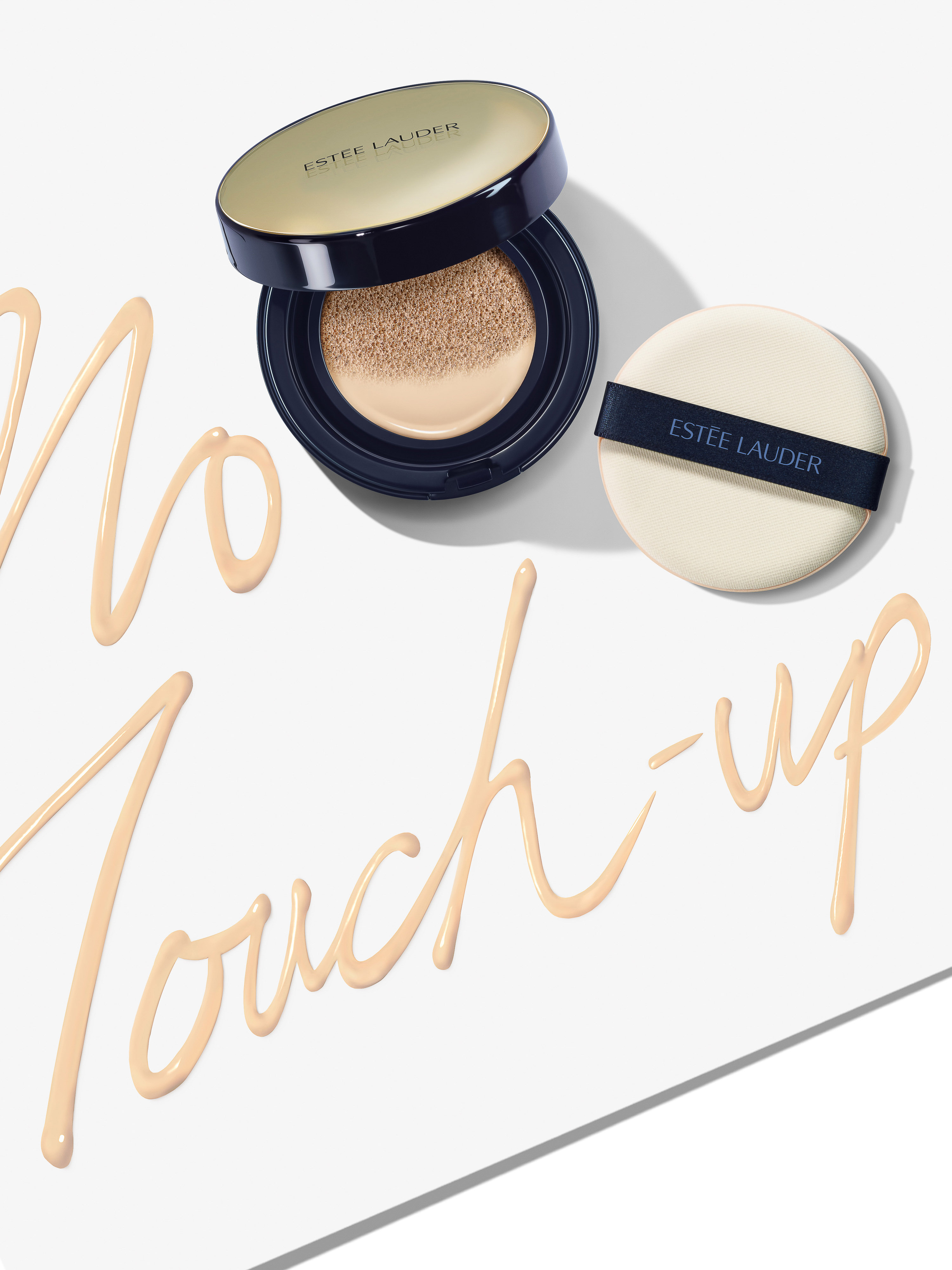 Close-up of Estee Lauder foundation in a black and gold compact with an applicator sponge and cream foundation swatches on white surface.
