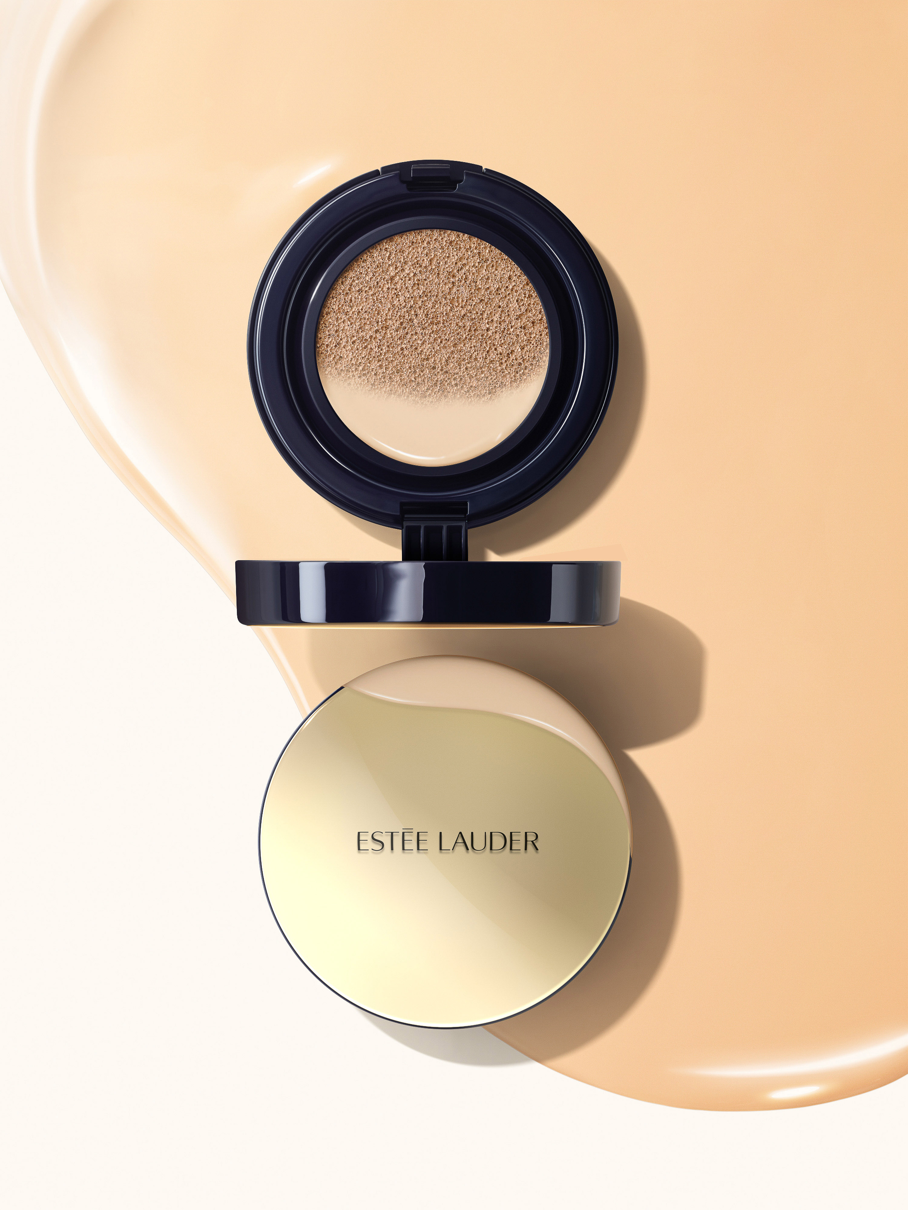 Estee Lauder compact is displayed against a beige backdrop. The compact features a gold lid and the brand name in black.