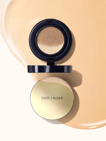 Estee Lauder compact is displayed against a beige backdrop. The compact features a gold lid and the brand name in black.