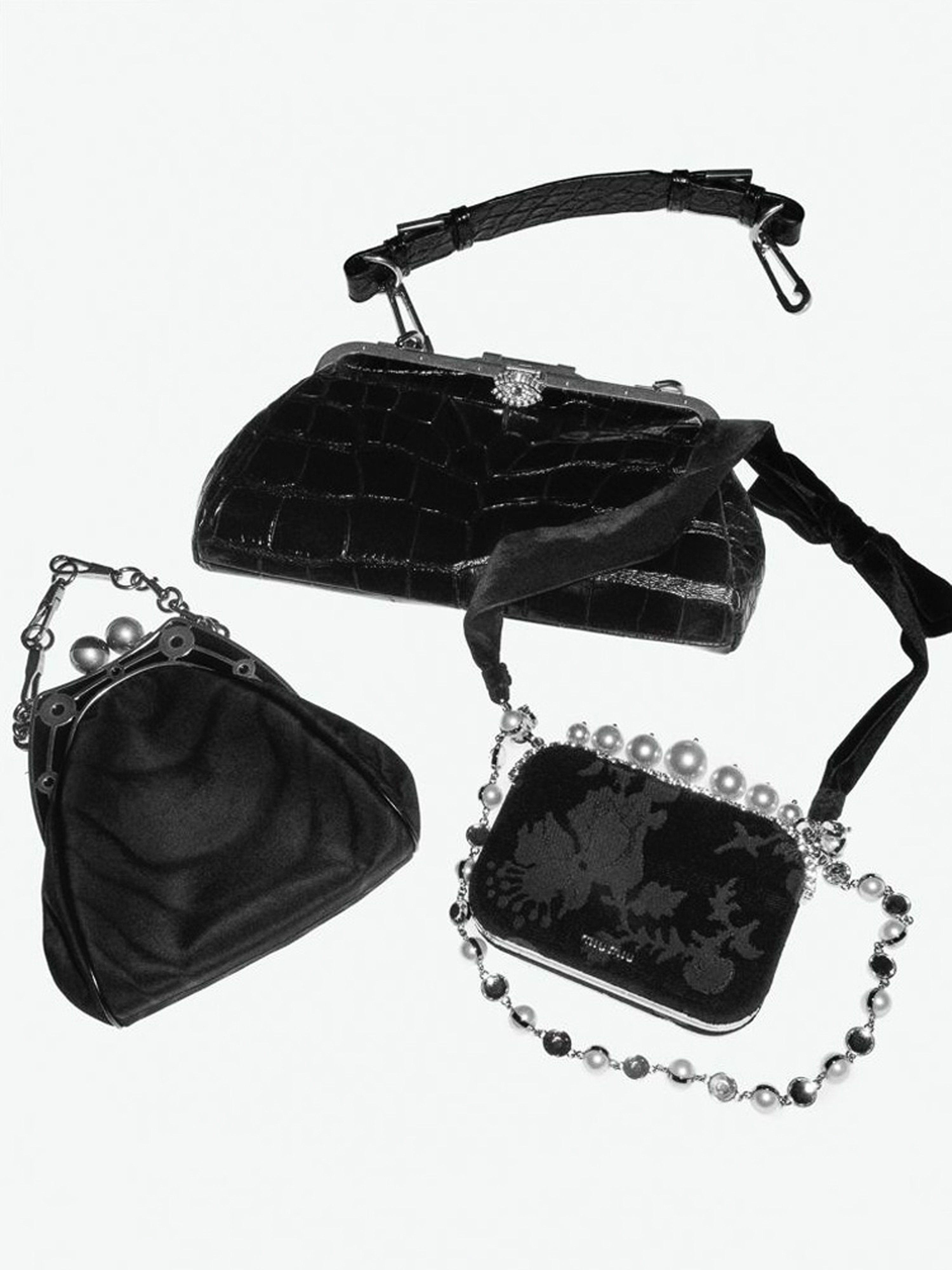 Three vintage black handbags are displayed on a white background. The purses feature different shapes, textures, and embellishments, creating a fashion still life.