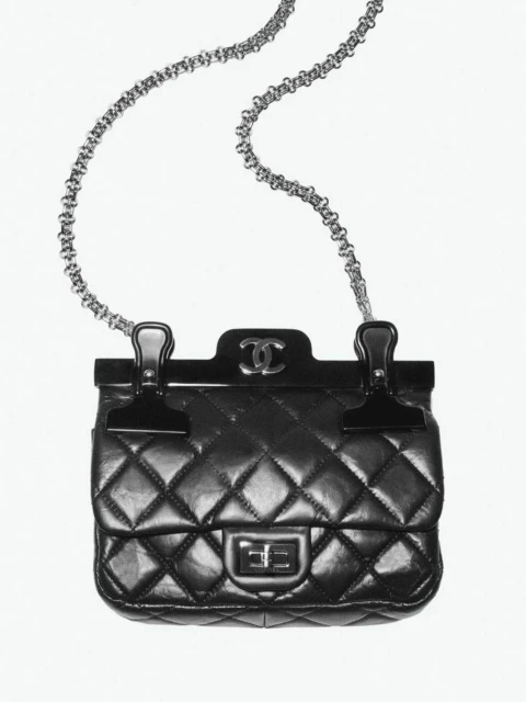 Black Chanel quilted handbag with metal chain strap and top clasp closure against a white background in a studio product shot.
