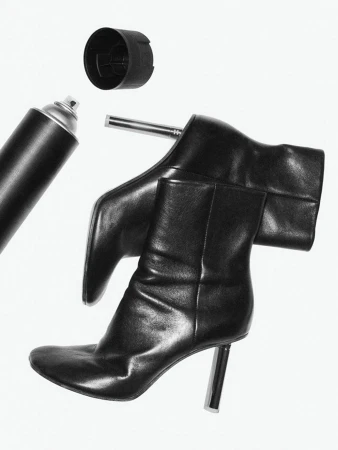 Stylized black and white still life photograph of shiny black high-heeled boots with a spray paint can and cap on a white backdrop.