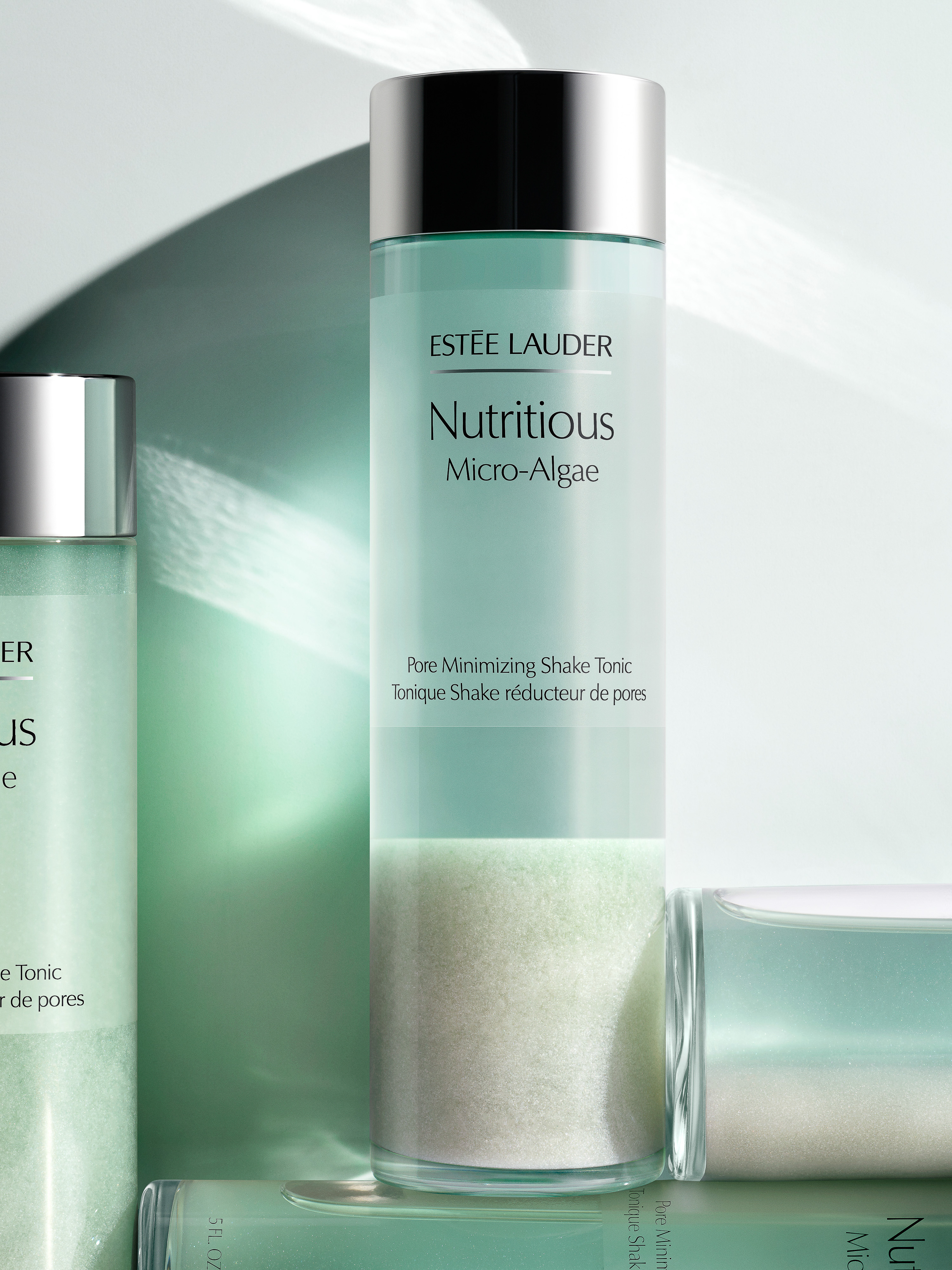 Estee Lauder Nutritious Micro-Algae pore minimizing tonic in a glass bottle with a silver lid on a light green surface.