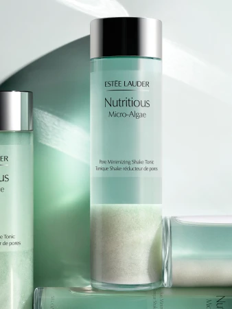 Estee Lauder Nutritious Micro-Algae pore minimizing tonic in a glass bottle with a silver lid on a light green surface.
