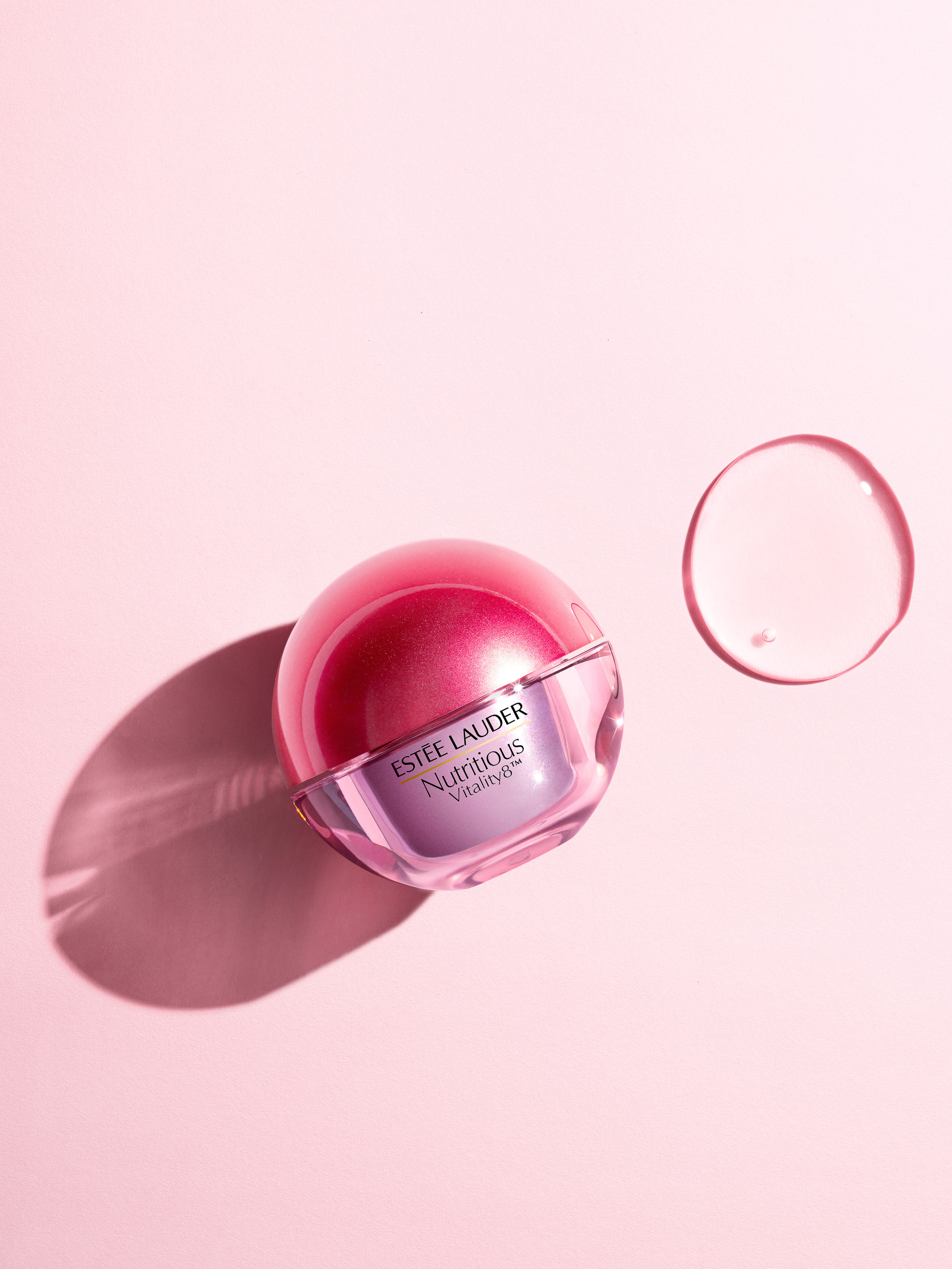 Estee Lauder Nutritious Vitality8 cream jar with a pink lid and clear gel droplet on a pink background in a beauty product shot.
