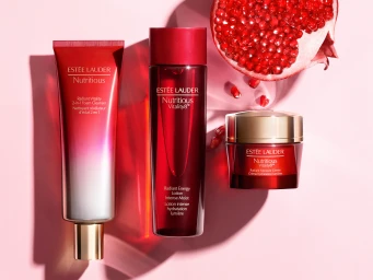 Estee Lauder Nutritious skincare products arranged with a halved pomegranate on a pink surface.