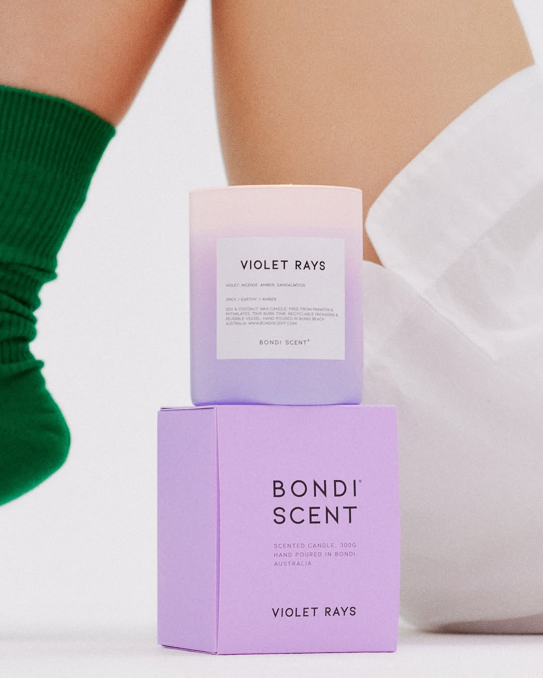 Candle and box from Bondi Scent, featuring the Violet Rays scent name and product information, against a white background with green socks.