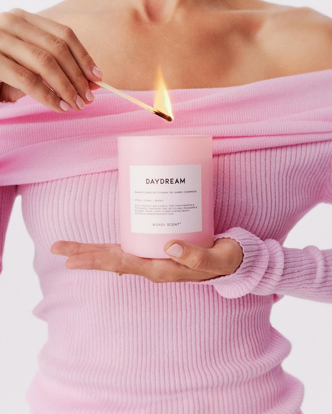 Woman in pink lighting a candle with a match. Soft, diffused light highlights the scene in a studio setting with minimal props.