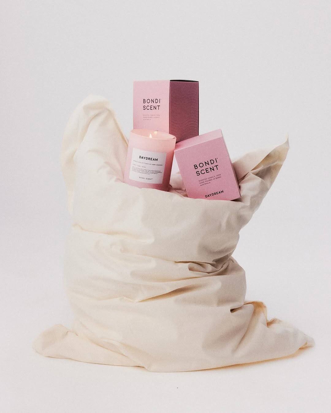 Still life product shot of a pink candle and packaging by Bondi Scent, resting in a wrinkled white fabric, against a white backdrop.