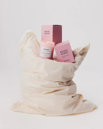 Still life product shot of a pink candle and packaging by Bondi Scent, resting in a wrinkled white fabric, against a white backdrop.