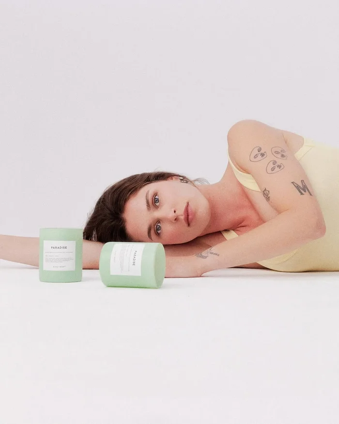 Woman in pale yellow top resting her head on a white surface next to two green candles from Bondi Scent