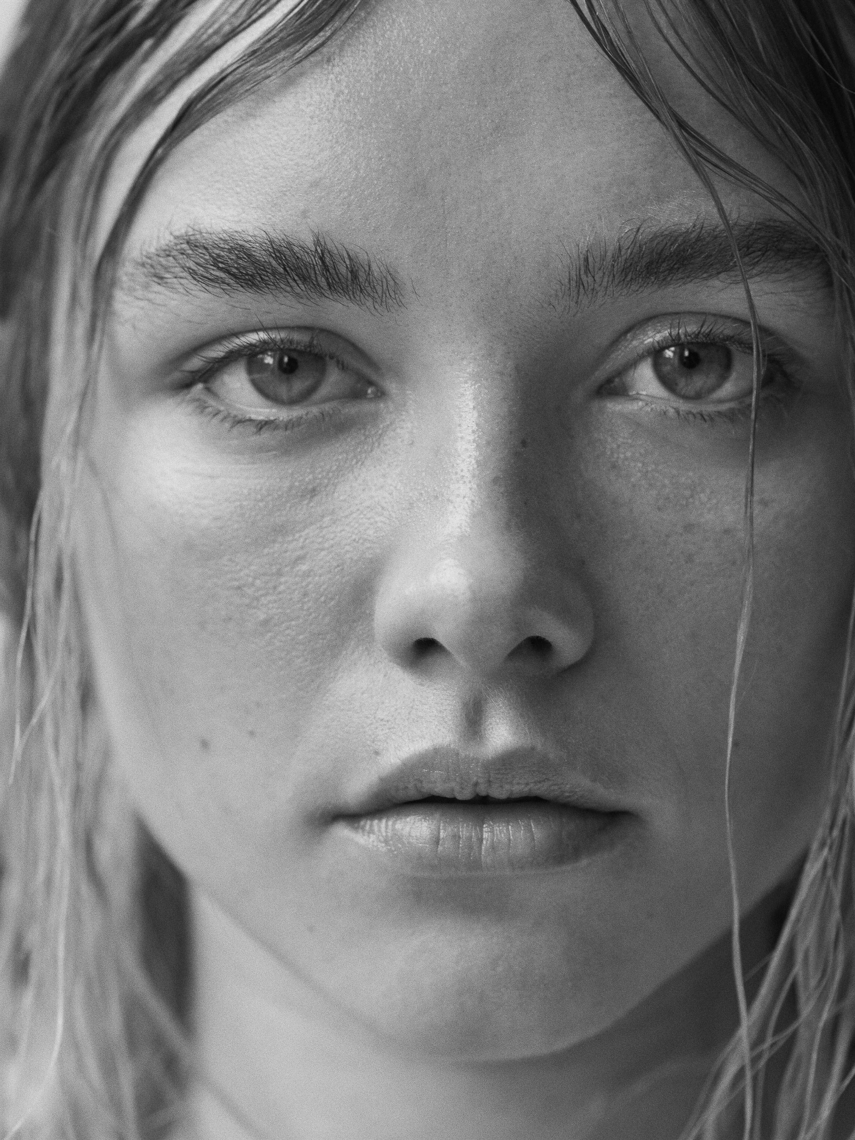 Striking black and white portrait of a young adult female with captivating eyes, natural makeup, and slightly damp hair framing her face.