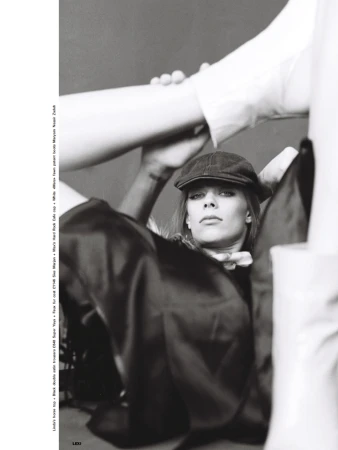 Monochrome portrait of a woman wearing a cap, staring at the camera with a serious expression, partially framed by blurry objects.