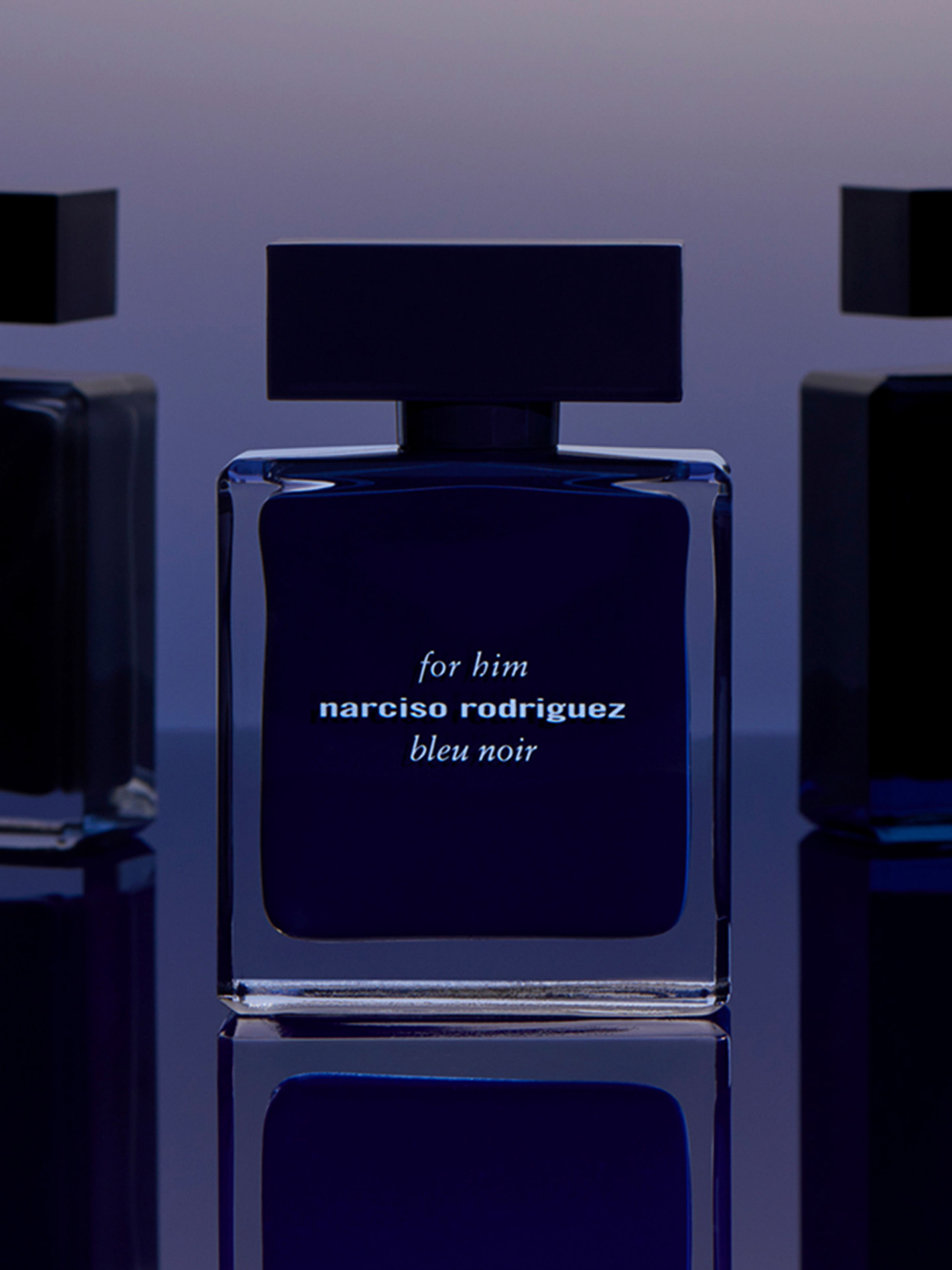Narciso Rodriguez 'bleu noir' fragrance bottle displayed on a reflective surface against a gradient blue background, product shot.
