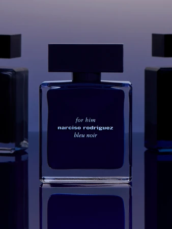 Narciso Rodriguez 'bleu noir' fragrance bottle displayed on a reflective surface against a gradient blue background, product shot.