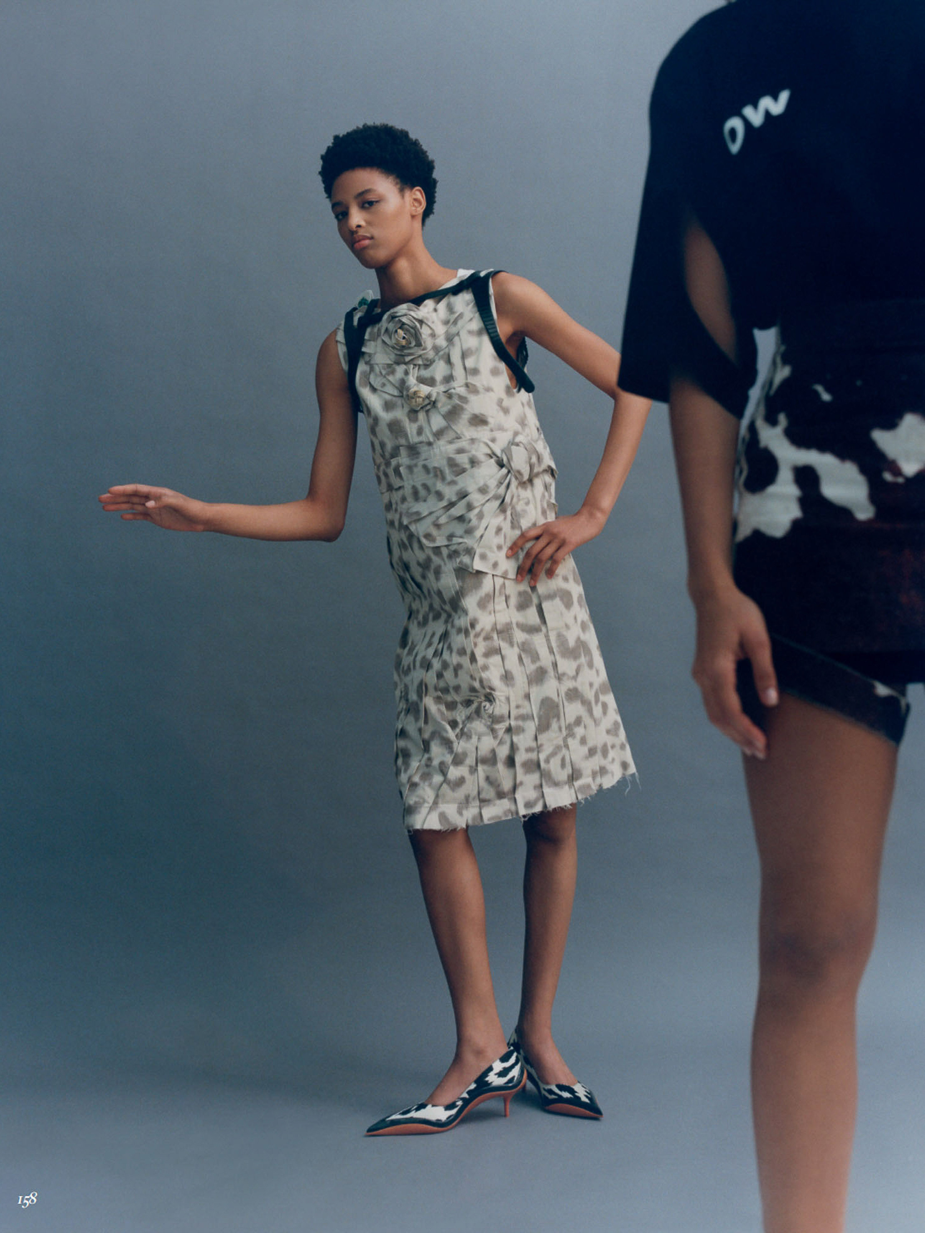 Two models pose in a photo studio, one in a patterned sleeveless dress and kitten heels, the other partially visible in a patterned top.
