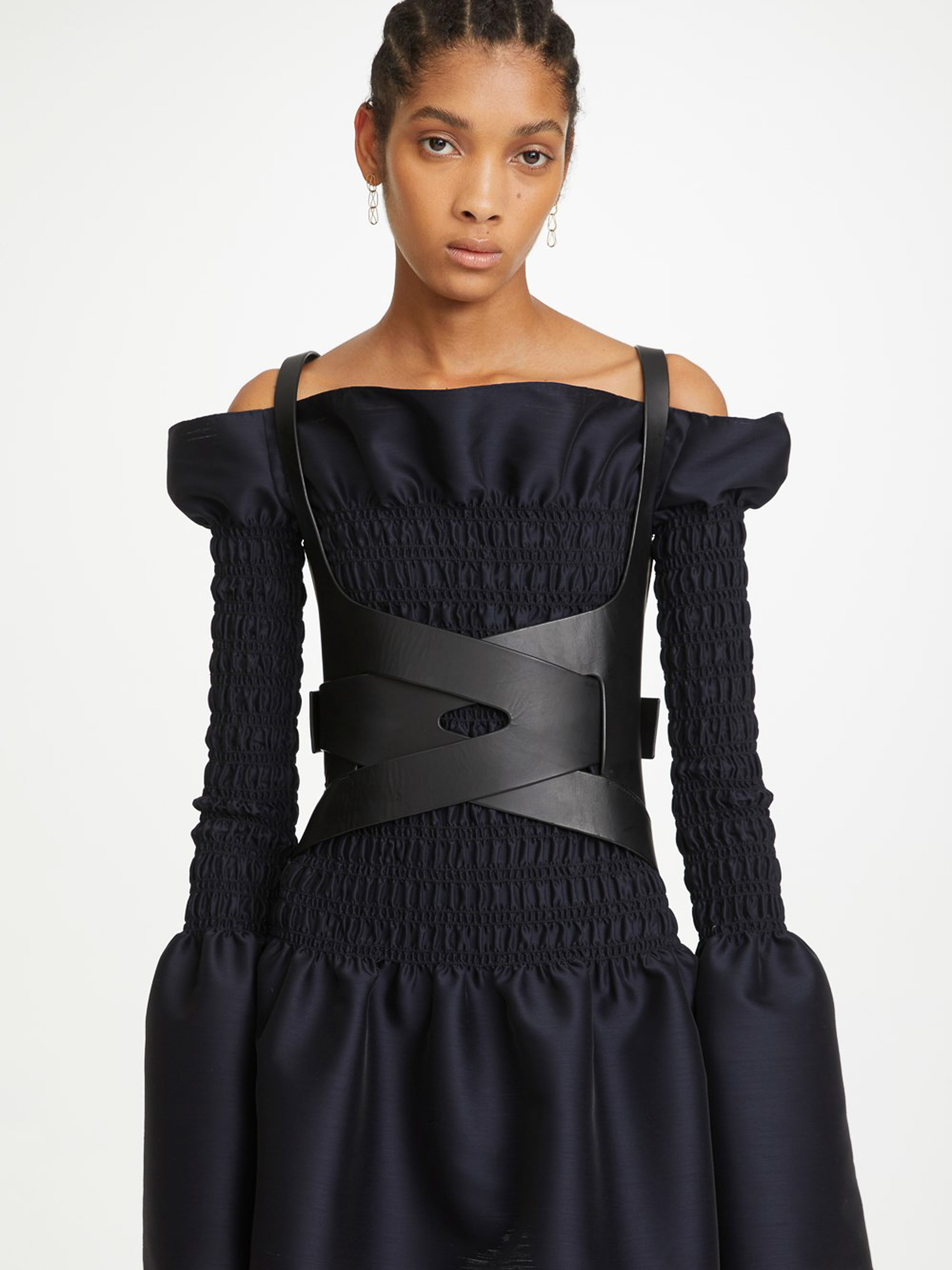 Fashion shot of a woman with braided hair wearing a black corset top and dress in a studio setting, showcasing modern apparel.