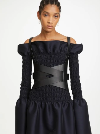 Fashion shot of a woman with braided hair wearing a black corset top and dress in a studio setting, showcasing modern apparel.