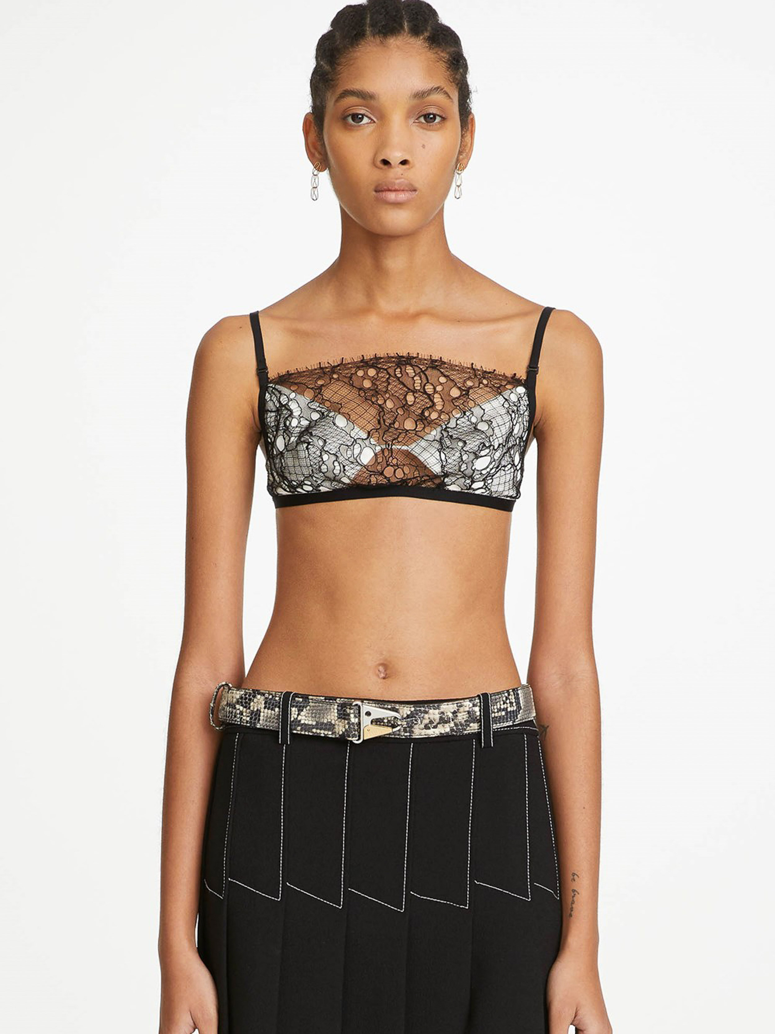 Portrait of a woman wearing a lace bra top, black skirt with white stitching, and patterned belt on a white backdrop.